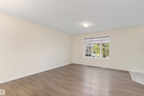 Spacious room featuring wood-finish flooring, light-toned walls, and a large window with roller shades - 336 Watt Boulevard, Edmonton, AB - Indoor