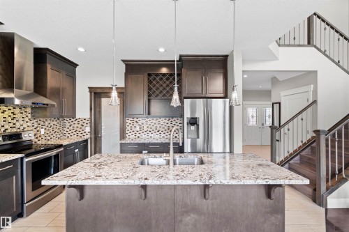 Kitchen featuring a large central island with an undermount sink and granite countertop, dark wood cabinetry, and stainless steel appliances including a refrigerator and range - 3807 Claxton Close, Edmonton, AB - Indoor Photo Showing Kitchen With Double Sink With Upgraded Kitchen