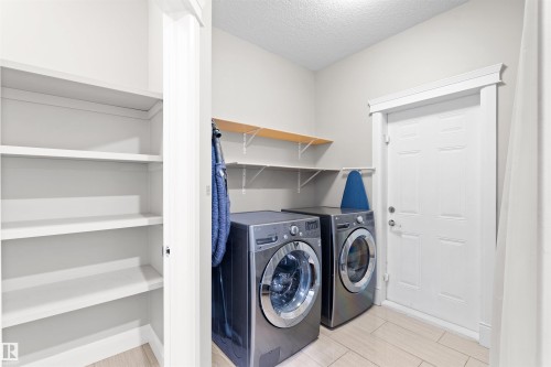 Laundry area featuring tiled flooring, built-in shelving, wall-mounted wooden shelving, and a paneled white door with trim - 3807 Claxton Close, Edmonton, AB - Indoor Photo Showing Laundry Room