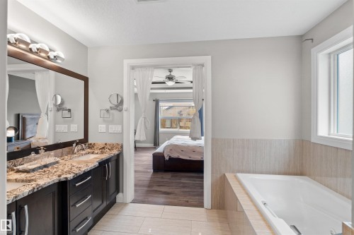 Bathroom featuring a dual vanity with a granite countertop, dark wood cabinetry, and a large mirror with integrated lighting - 3807 Claxton Close, Edmonton, AB - Indoor Photo Showing Bathroom