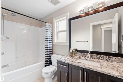 Bathroom featuring a dark wood vanity with a light granite-style countertop, undermount sink, and chrome faucet - 3807 Claxton Close, Edmonton, AB - Indoor Photo Showing Bathroom