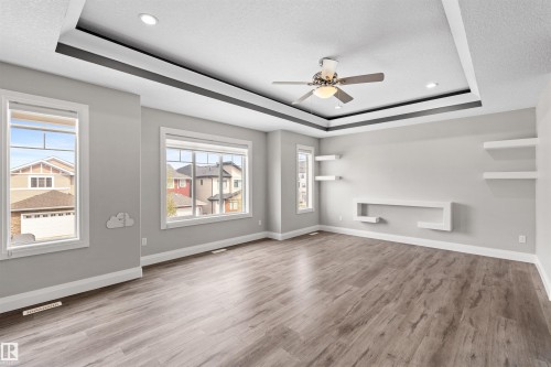Spacious room featuring wood-finish flooring, multiple windows, a tray ceiling with recessed lighting and a ceiling fan, and built-in wall shelving - 3807 Claxton Close, Edmonton, AB - Indoor Photo Showing Other Room