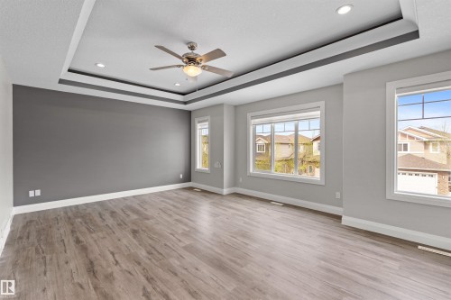 Spacious room featuring a tray ceiling with recessed lighting and a ceiling fan, wood-finish flooring, large windows, and neutral wall tones - 3807 Claxton Close, Edmonton, AB - Indoor Photo Showing Other Room