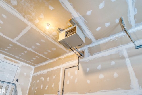Garage interior featuring unpainted drywall, overhead heating unit, exposed utility piping, and a white interior door - 3807 Claxton Close, Edmonton, AB - Indoor Photo Showing Other Room