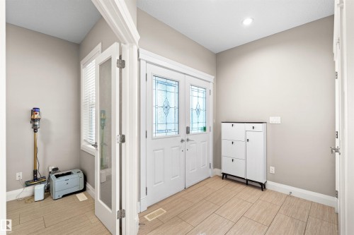 Inviting entry with double doors featuring decorative glass inserts, light-toned wall paint, and wood-finish tile flooring - 3807 Claxton Close, Edmonton, AB - Indoor Photo Showing Other Room