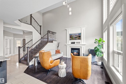 Two-story living area featuring a prominent fireplace with a detailed mantel, tall windows, and a multi-level staircase with dark wood railings and metal balusters - 3807 Claxton Close, Edmonton, AB - Indoor With Fireplace