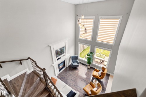 Two-story living area featuring dark wood-finish flooring, a white mantel fireplace, and a striking light fixture - 3807 Claxton Close, Edmonton, AB - Indoor Photo Showing Other Room