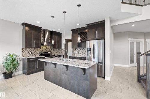Modern kitchen featuring dark wood cabinetry, stainless steel appliances, a multi-tone tile backsplash, and a central island with a light-colored countertop - 3807 Claxton Close, Edmonton, AB - Indoor Photo Showing Kitchen With Upgraded Kitchen