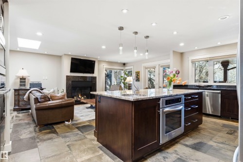 Open-concept kitchen and living area featuring a large center island with integrated stainless steel oven, stone countertop, and pendant lighting - 9010 120 Street, Edmonton, AB - Indoor Photo Showing Kitchen With Fireplace With Upgraded Kitchen