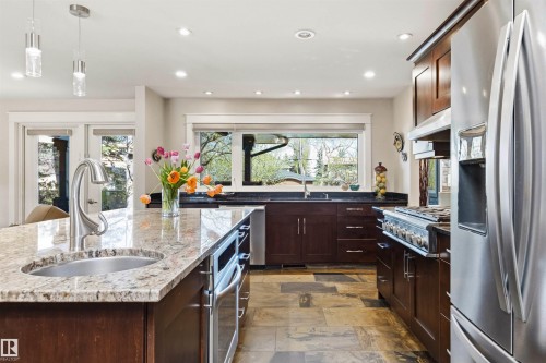Kitchen featuring a central island with an undermount sink and stone countertop, stainless steel appliances, rich wood cabinetry, and recessed lighting - 9010 120 Street, Edmonton, AB - Indoor Photo Showing Kitchen With Upgraded Kitchen
