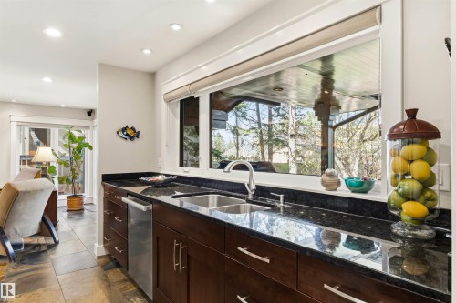 Kitchen workstation featuring dark wood cabinetry, dark stone countertops, and a dual basin stainless steel sink with a gooseneck faucet - 9010 120 Street, Edmonton, AB - Indoor Photo Showing Kitchen With Double Sink