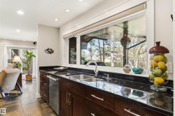 Kitchen workstation featuring dark wood cabinetry, dark stone countertops, and a dual basin stainless steel sink with a gooseneck faucet - 