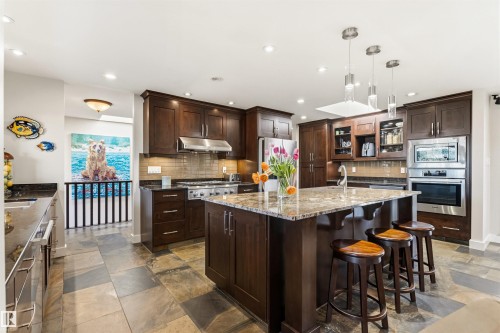 Spacious kitchen featuring dark wood cabinetry, a large center island with a stone countertop, recessed lighting, and stainless steel appliances - 9010 120 Street, Edmonton, AB - Indoor Photo Showing Kitchen With Upgraded Kitchen