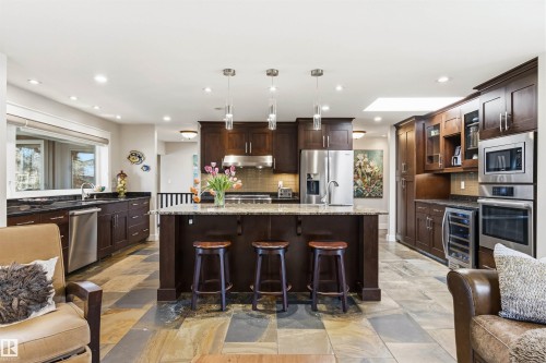 Gourmet kitchen featuring a central island with integrated seating, stainless steel appliances, dark wood cabinetry, and multi-toned slate flooring - 9010 120 Street, Edmonton, AB - Indoor Photo Showing Kitchen With Upgraded Kitchen