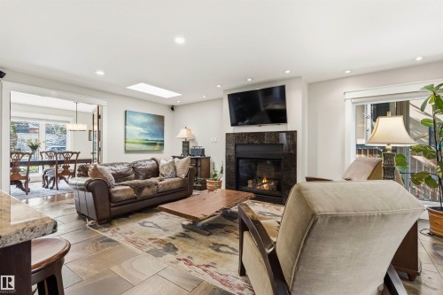 Living area featuring large format stone tile flooring, a dark stone fireplace surround, an inset fireplace, and recessed lighting - 9010 120 Street, Edmonton, AB - Indoor Photo Showing Living Room With Fireplace