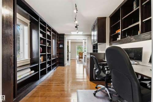 Dedicated office space featuring extensive dark wood built-in shelving, light wood-finish flooring, and track lighting - 9010 120 Street, Edmonton, AB - Indoor Photo Showing Office