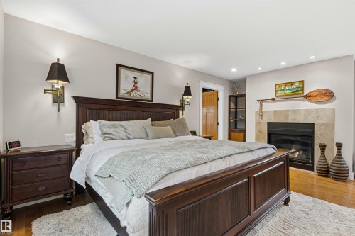 Spacious bedroom featuring wood-finish flooring, a built-in fireplace with a stone surround, recessed lighting, and wall sconces - 9010 120 Street, Edmonton, AB - Indoor Photo Showing Bedroom