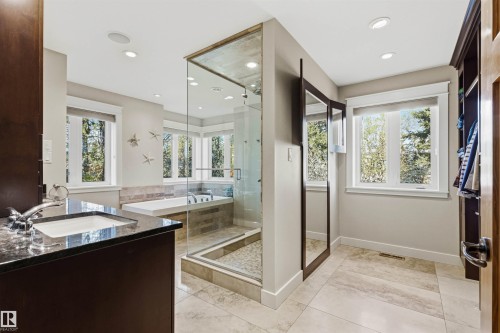 Spacious bathroom featuring a glass-enclosed shower, built-in soaking tub, vanity with undermount sink and dark countertop, and light-toned tile flooring - 9010 120 Street, Edmonton, AB - Indoor Photo Showing Bathroom