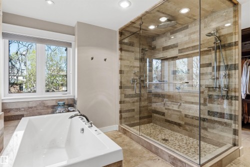 Spacious bathroom featuring a large soaking tub with window, a glass-enclosed shower with tile surround, a rain showerhead, a handheld shower fixture, and recessed lighting - 9010 120 Street, Edmonton, AB - Indoor Photo Showing Bathroom