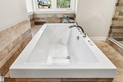 White rectangular soaking tub with polished chrome fixtures, integrated controls, and a window above - 