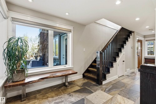 Entryway featuring stone tile flooring, a dark wood staircase with spindle railing, and a window with a built-in live-edge wood bench - 9010 120 Street, Edmonton, AB - Indoor Photo Showing Other Room