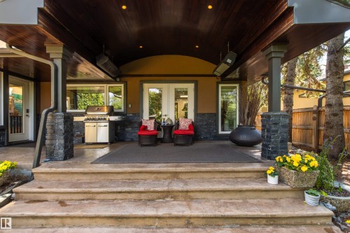 Covered outdoor patio featuring a wood-finish ceiling, recessed lighting, and stone veneer columns - 9010 120 Street, Edmonton, AB - Outdoor With Deck Patio Veranda With Exterior