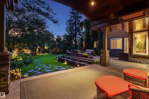 Expansive outdoor living area featuring a covered patio with integrated overhead heating, a multi-level stone-clad patio, a stepping stone pathway, a manicured lawn, and mature landscaping with accent lighting - 9010 120 Street, Edmonton, AB - Outdoor With Deck Patio Veranda