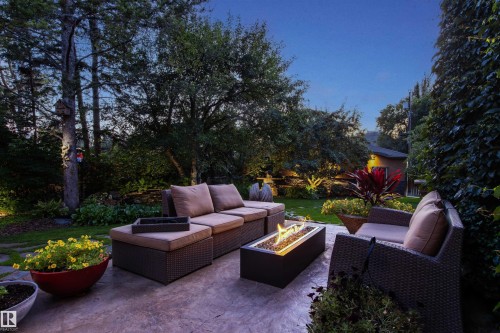 Expansive patio featuring stamped concrete, a built-in fire pit, mature landscaping with accent lighting, a stone retaining wall, and established perimeter plantings - 9010 120 Street, Edmonton, AB - Outdoor
