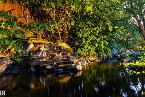 Landscaped water feature with a multi-tiered stone waterfall, surrounded by mature foliage - 9010 120 Street, Edmonton, AB - Outdoor