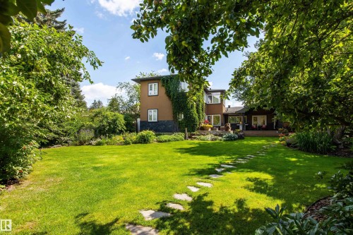 Expansive backyard featuring a manicured lawn, established garden beds, mature trees, and a flagstone pathway - 9010 120 Street, Edmonton, AB - Outdoor