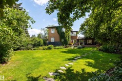 Expansive backyard featuring a manicured lawn, established garden beds, mature trees, and a flagstone pathway - 