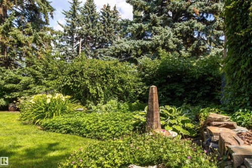 Landscaped garden featuring mature trees, diverse plantings, a stone obelisk, and a natural stone retaining wall - 9010 120 Street, Edmonton, AB - Outdoor