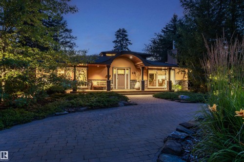 Curved paved driveway leading to a residence featuring a stucco and stone facade, covered entry with wood columns, and integrated landscaping with mature trees and uplighting - 9010 120 Street, Edmonton, AB - Outdoor With Deck Patio Veranda