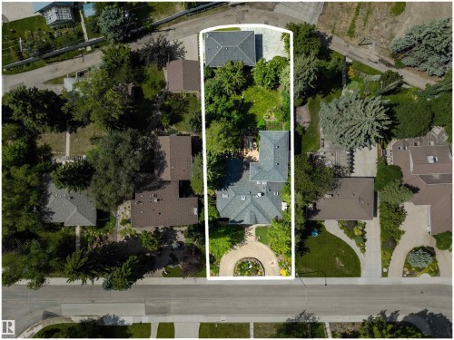Expansive property featuring a main residence with a gray shingle roof, a detached structure with a similar roofline, a circular front garden with a central planting, mature trees providing ample shade, and a paved driveway - 9010 120 Street, Edmonton, AB - Outdoor With View
