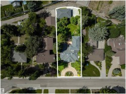 Expansive property featuring a main residence with a gray shingle roof, a detached structure with a similar roofline, a circular front garden with a central planting, mature trees providing ample shade, and a paved driveway - 