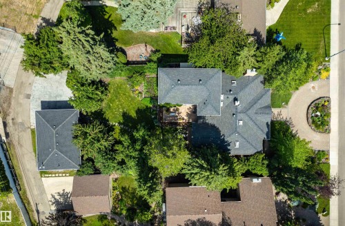 Expansive property featuring a multi-gabled main residence with a dark shingle roof, a separate accessory dwelling unit, a circular driveway with a landscaped center island, a paved side driveway, and extensive mature trees and greenery - 9010 120 Street, Edmonton, AB - Outdoor With View