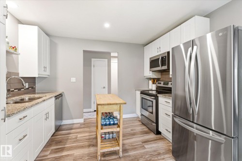 Modern kitchen featuring stainless steel appliances, white cabinetry, granite-finish countertops, wood-finish flooring, and a tiled backsplash - 111 Grosvenor Boulevard, St. Albert, AB - Indoor Photo Showing Kitchen With Stainless Steel Kitchen With Double Sink