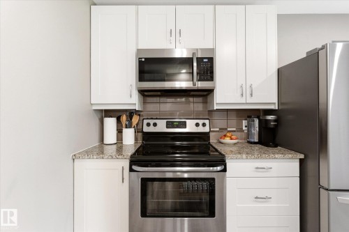 Kitchen featuring white shaker-style cabinetry, stainless steel appliances, granite-finish countertops, and a tiled backsplash - 111 Grosvenor Boulevard, St. Albert, AB - Indoor Photo Showing Kitchen