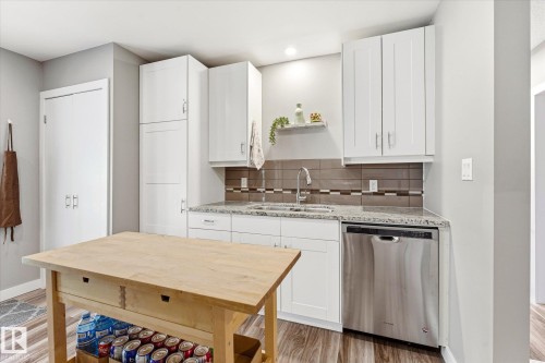 Kitchen featuring white cabinetry, a stainless steel dishwasher, a double basin sink with a high-arc faucet, granite countertops, and wood-finish flooring - 111 Grosvenor Boulevard, St. Albert, AB - Indoor Photo Showing Kitchen With Double Sink