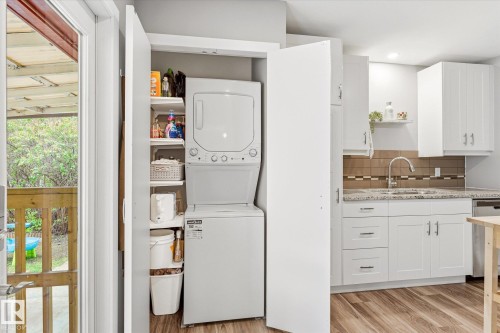 Dedicated laundry closet featuring a stackable washer and dryer, white shelving, and adjacent to a kitchen with white cabinetry, granite-finish countertops, and a tiled backsplash - 111 Grosvenor Boulevard, St. Albert, AB - Indoor Photo Showing Laundry Room