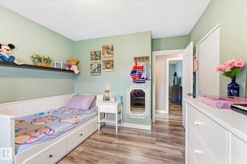 Room featuring wood-finish flooring, a built-in wall shelf, light green walls, a white dresser with multiple drawers, and white trim - 111 Grosvenor Boulevard, St. Albert, AB - Indoor Photo Showing Bedroom
