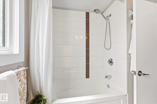 White tile shower surround with a vertical brown accent tile strip - 111 Grosvenor Boulevard, St. Albert, AB - Indoor Photo Showing Bathroom