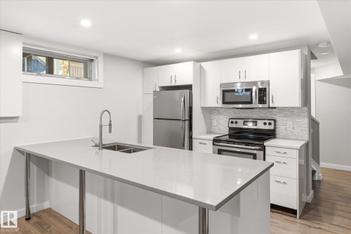 Modern kitchen featuring a large island with an undermount sink, stainless steel appliances, white cabinetry, and wood-finish flooring - 111 Grosvenor Boulevard, St. Albert, AB - Indoor Photo Showing Kitchen With Stainless Steel Kitchen With Double Sink
