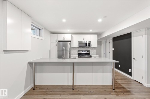 Modern kitchen featuring stainless steel appliances, white cabinetry, a large kitchen island with seating, a subway tile backsplash, and wood-finish flooring - 111 Grosvenor Boulevard, St. Albert, AB - Indoor Photo Showing Kitchen