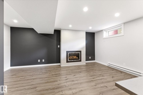 Spacious room featuring wood-finish flooring and a central fireplace with a tiled surround - 111 Grosvenor Boulevard, St. Albert, AB - Indoor With Fireplace