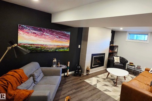 Living area featuring a floor-to-ceiling tiled fireplace with a black framed insert, wood-finish flooring, recessed lighting, and a built-in shelving unit - 111 Grosvenor Boulevard, St. Albert, AB - Indoor With Fireplace