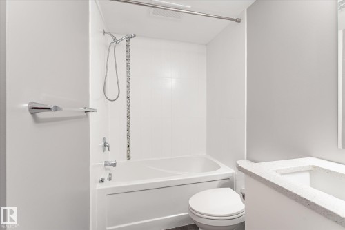Bathroom featuring a white bathtub, ceramic tile surround with a mosaic accent, chrome fixtures, and a white vanity with a speckled countertop - 111 Grosvenor Boulevard, St. Albert, AB - Indoor Photo Showing Bathroom