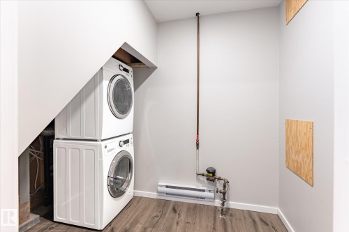 Dedicated laundry area featuring a stacked washer and dryer, wood-finish flooring, and light-toned walls - 111 Grosvenor Boulevard, St. Albert, AB - Indoor Photo Showing Laundry Room