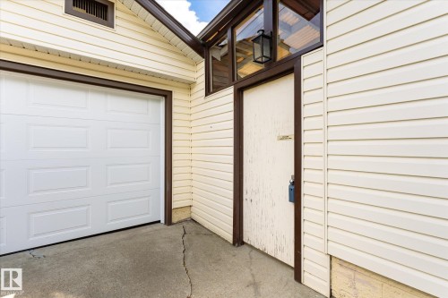 Exterior featuring cream-colored horizontal siding, a white panel garage door, brown trim accents, and an exterior light fixture - 111 Grosvenor Boulevard, St. Albert, AB - Outdoor With Exterior