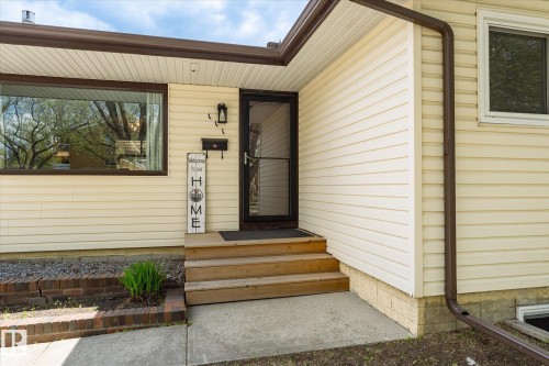 Exterior featuring light-toned horizontal siding, dark brown trim, and a prominent front door with a storm door - 111 Grosvenor Boulevard, St. Albert, AB - Outdoor With Exterior